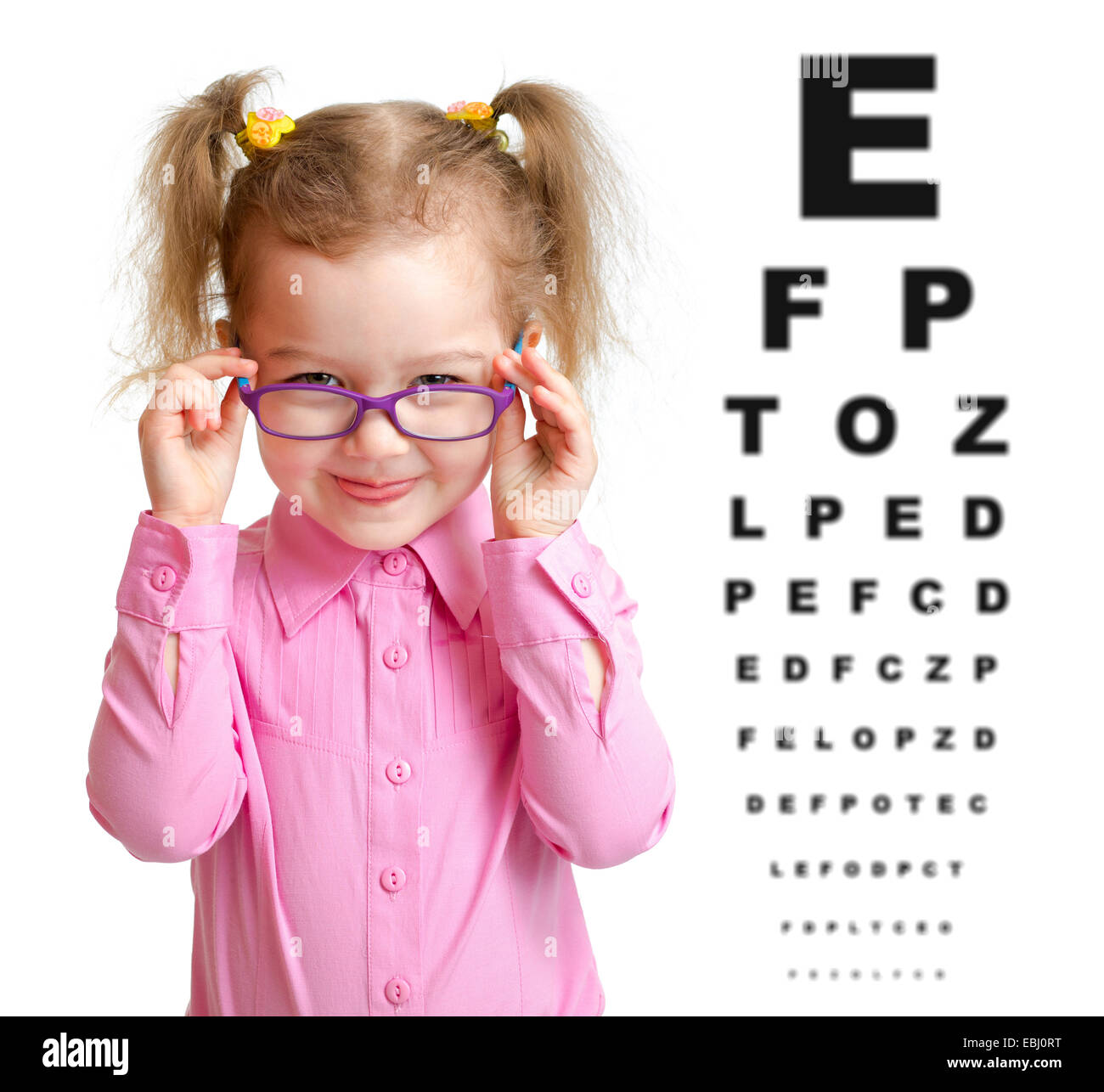 Smiling girl putting on glasses with blurry eye chart behind her Stock Photo