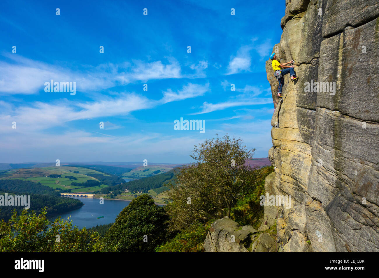 Rock climber in yellow on Bamford Edge, Derbyshire, Peak District, with Ladybower Reservoir behind Stock Photo