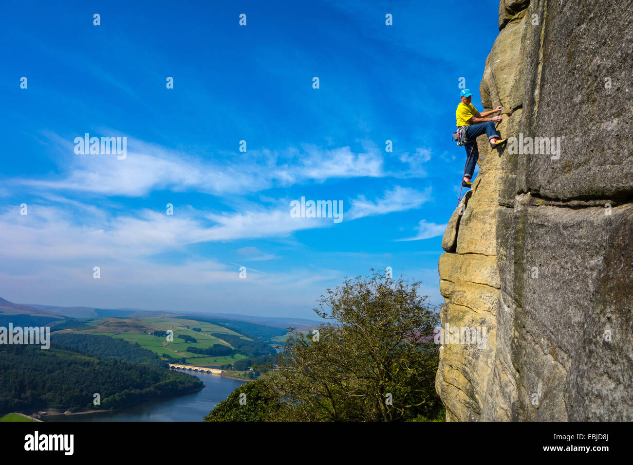 Rock climber in yellow on Bamford Edge, Derbyshire, Peak District, with Ladybower Reservoir behind Stock Photo