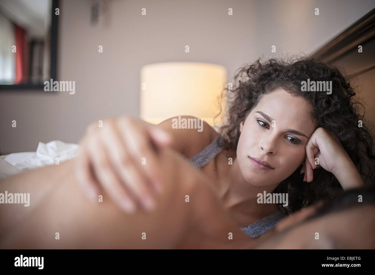 Young woman in bed with hand on man's shoulder Stock Photo