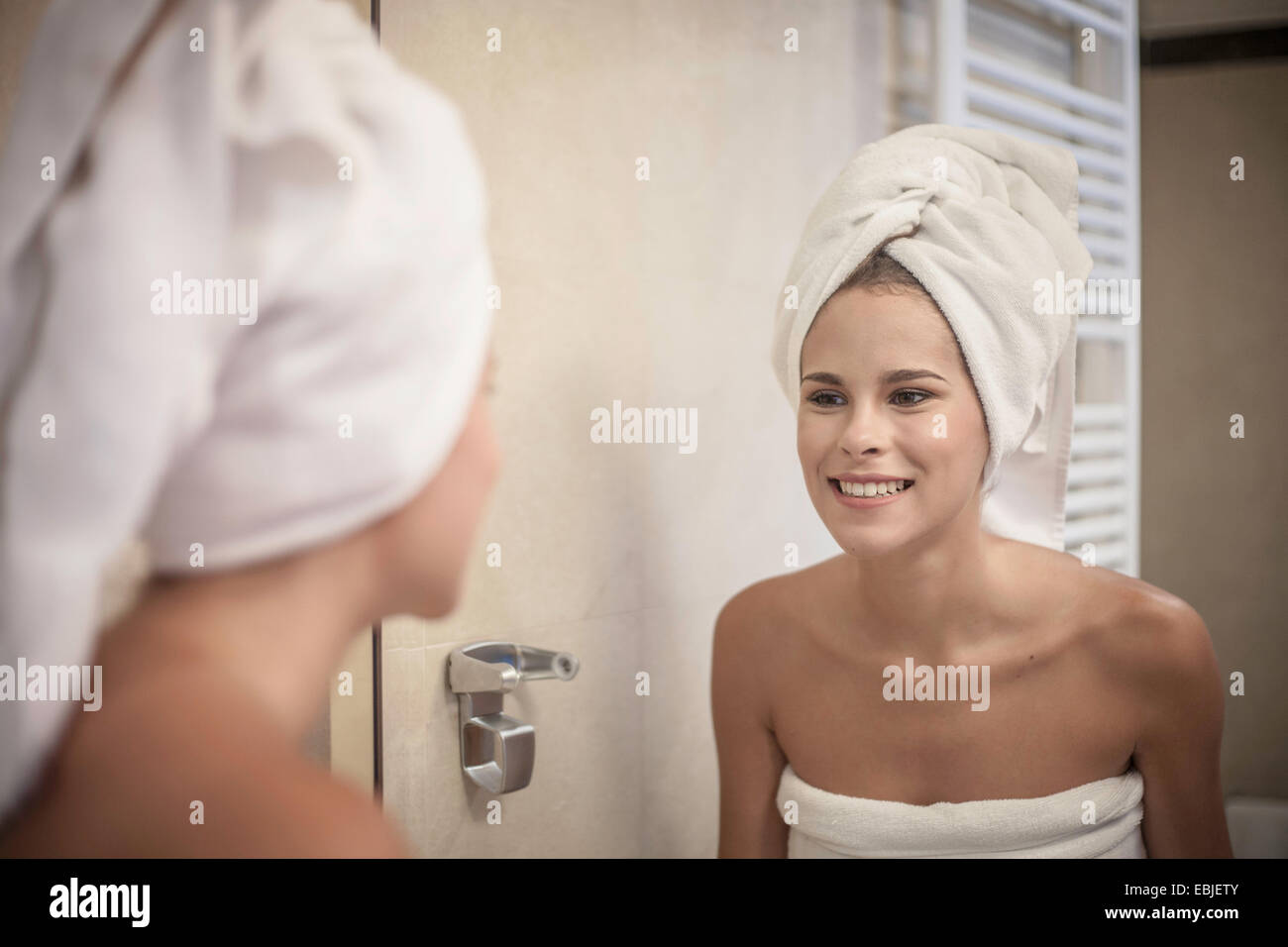 Young woman wearing towel on head looking at reflection in mirror Stock