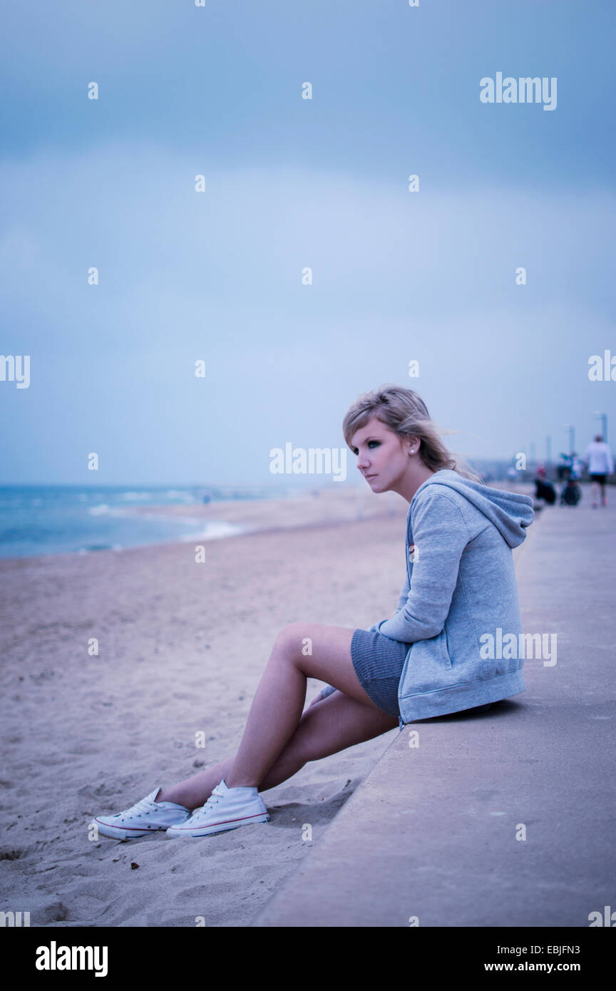 Young woman sitting on sea wall, looking out to sea Stock Photo - Alamy