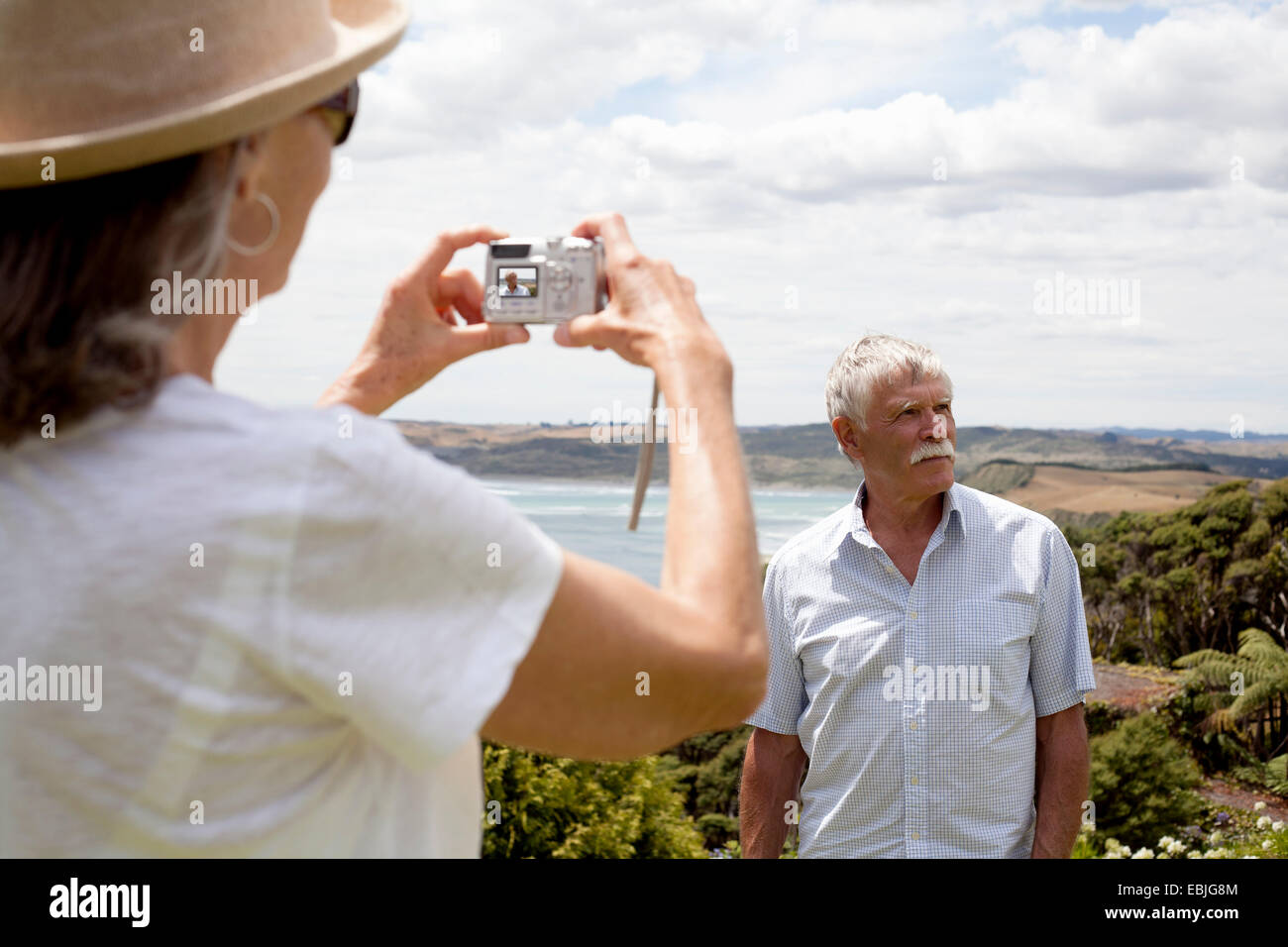 Wife photographing husband, ocean in background, Raglan, New Zealand Stock Photo