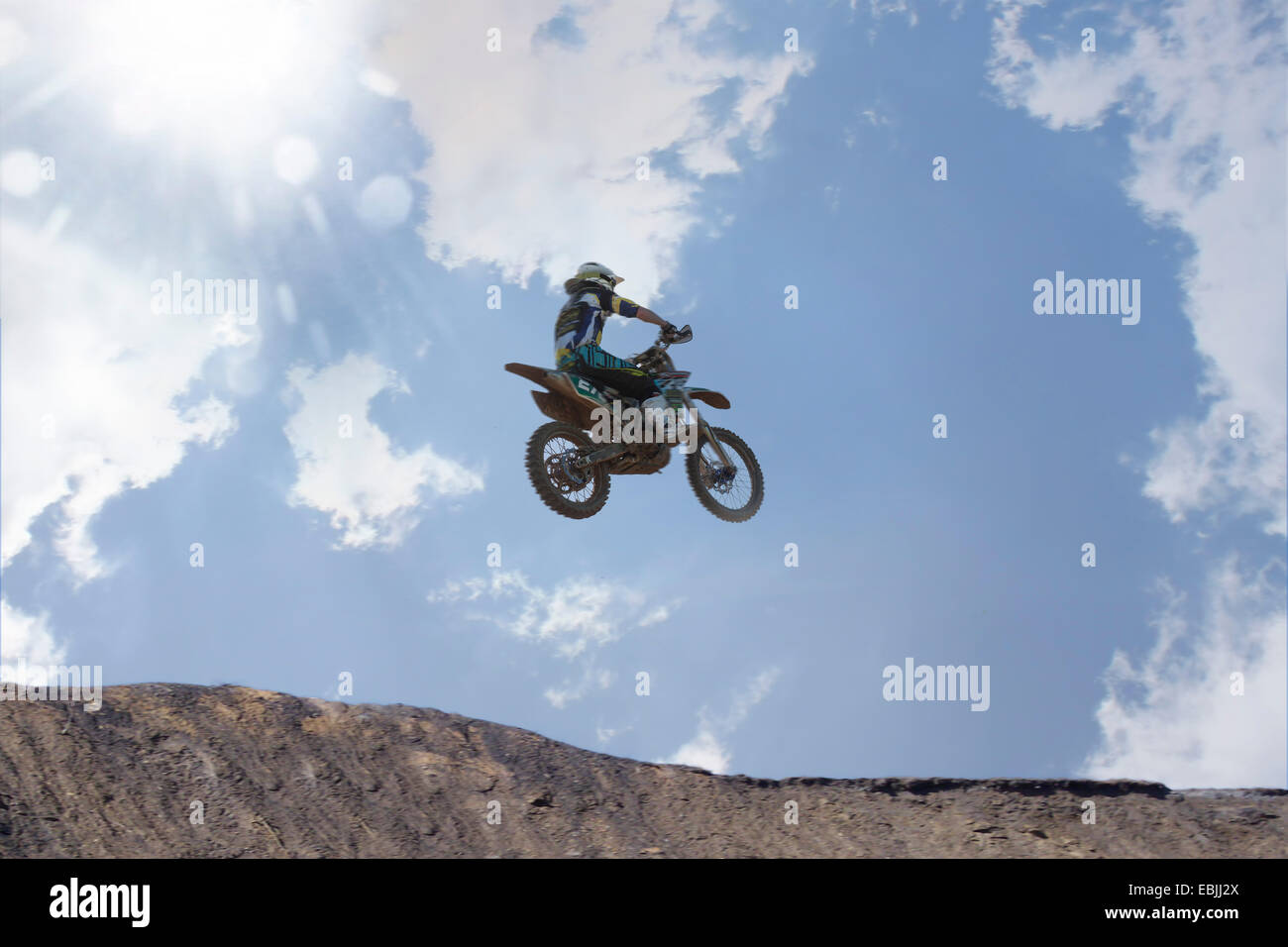 Silhouetted young male motocross racer jumping over mud hill Stock Photo