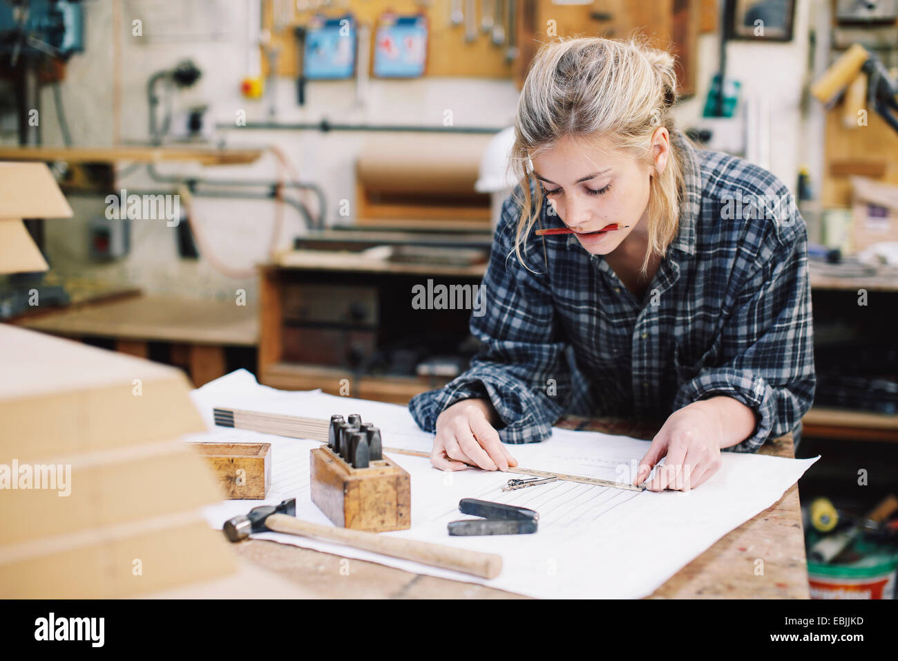 Young craftswoman measuring blueprint on workbench in pipe organ workshop Stock Photo