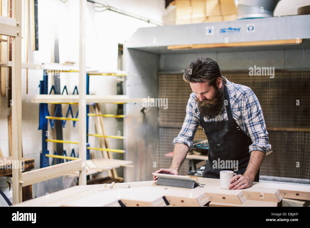 Cropped shot of mid adult craftsman using digital tablet in organ workshop Stock Photo