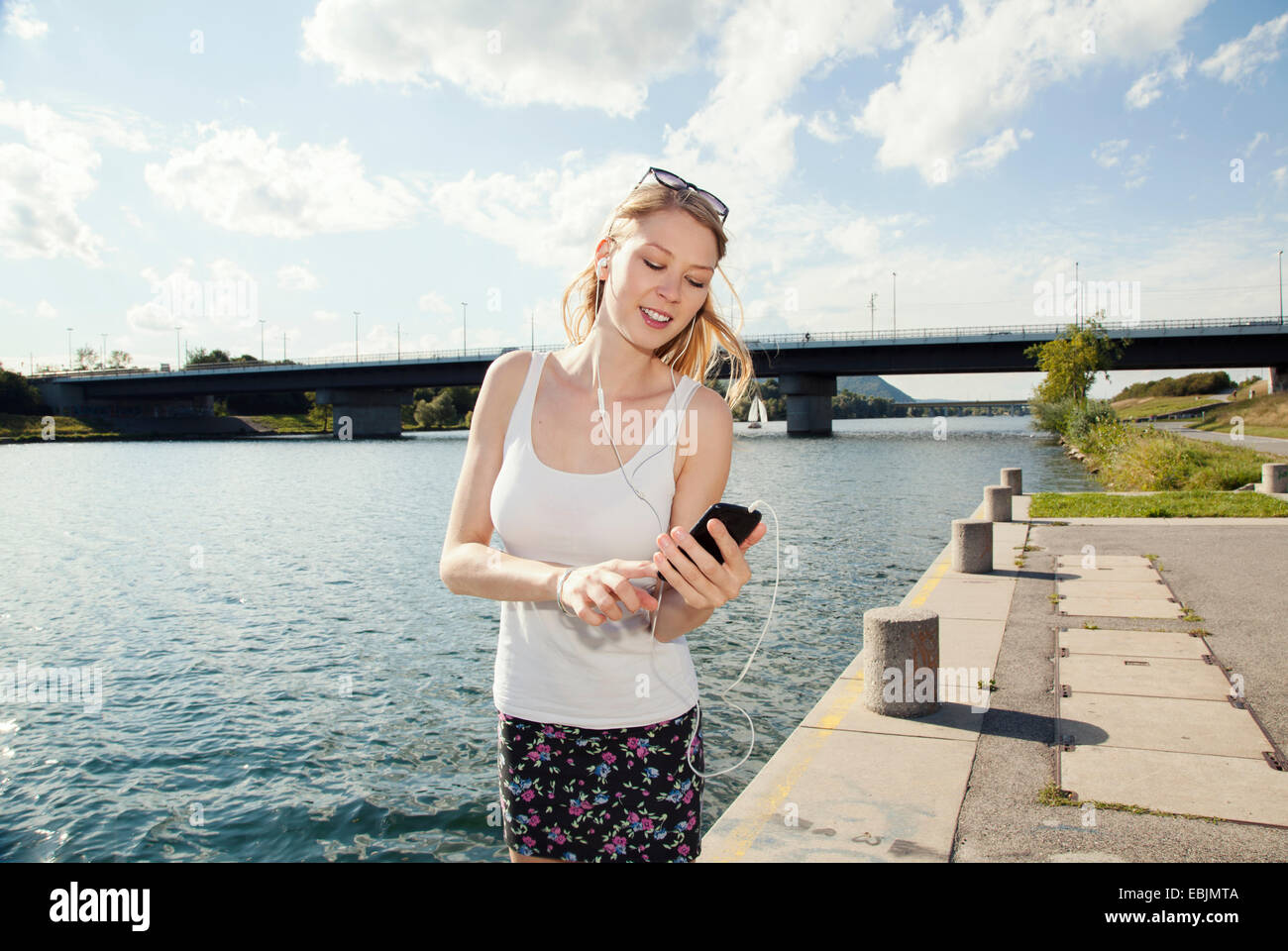 Young woman texting on smartphone on Danube Island riverside, Vienna, Austria Stock Photo