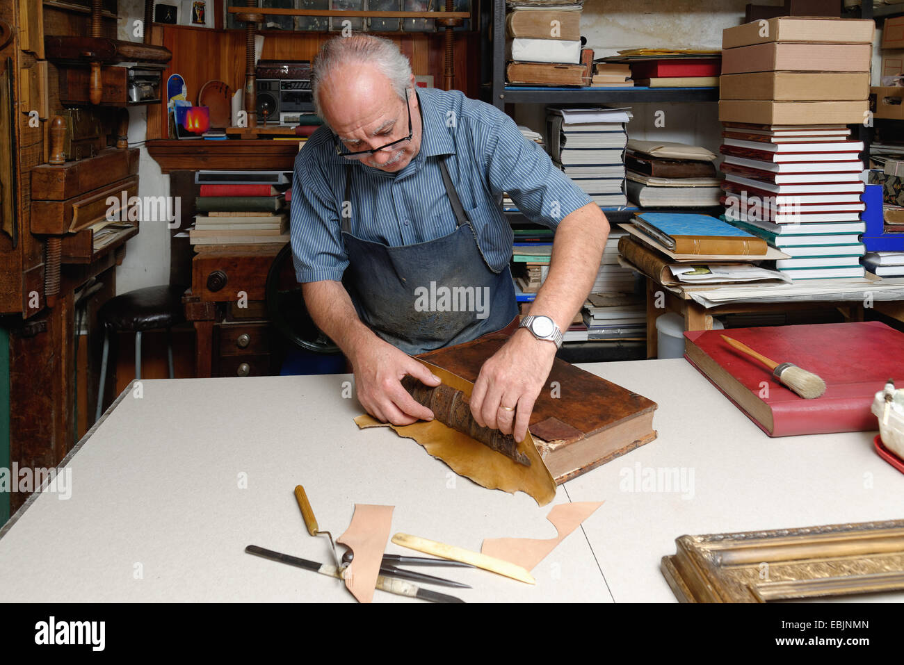 Senior man repairing antique book spine in traditional bookbinding
