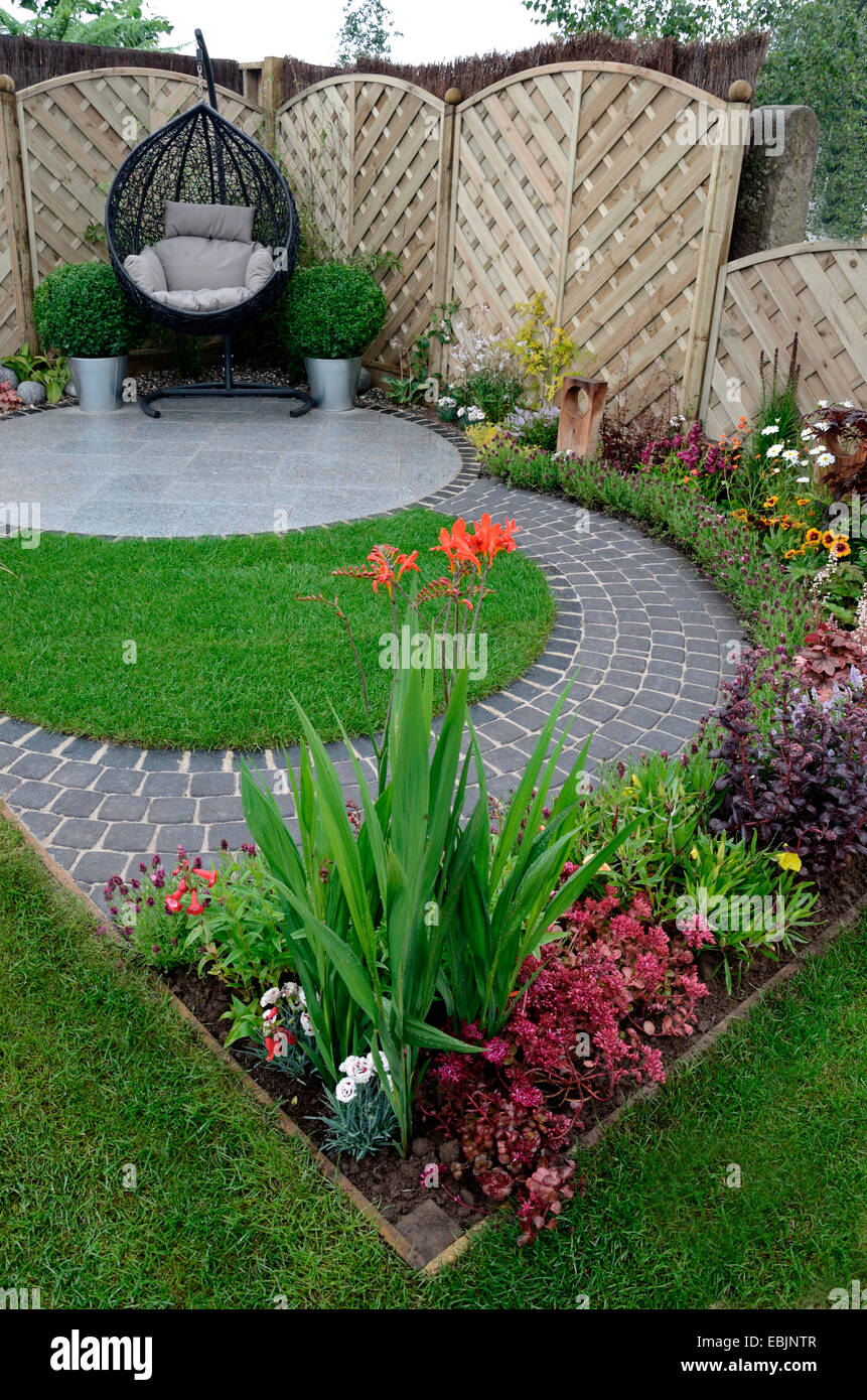 A garden design based on flowing curves around a patio area with a hanging cane chair Stock Photo