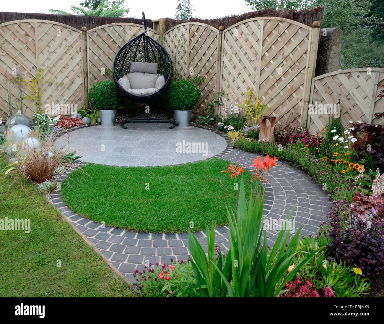 A garden design based on flowing curves around a patio area with a hanging cane chair Stock Photo