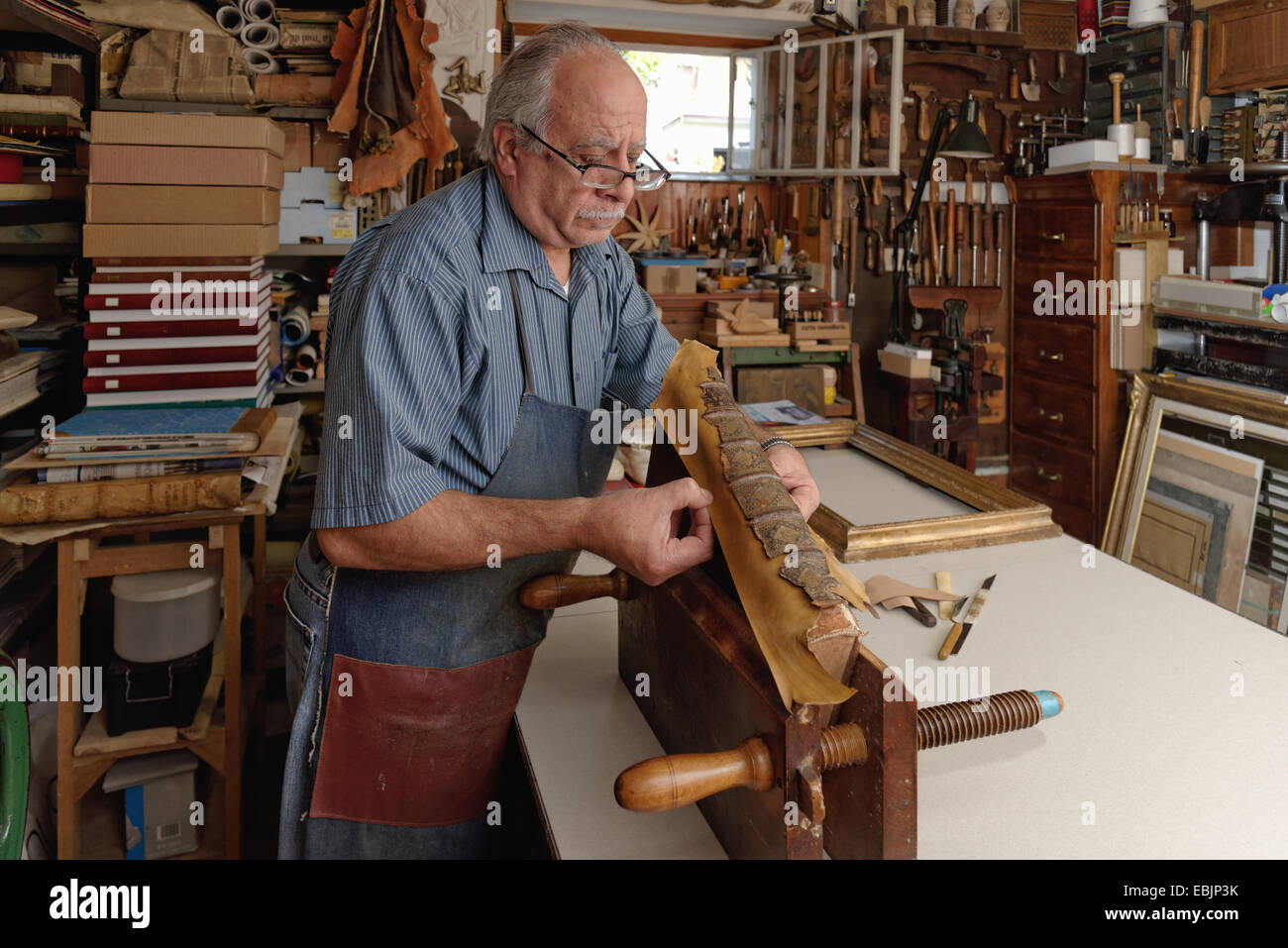 Senior man repairing fragile antique book spine in traditional bookbinding workshop Stock Photo