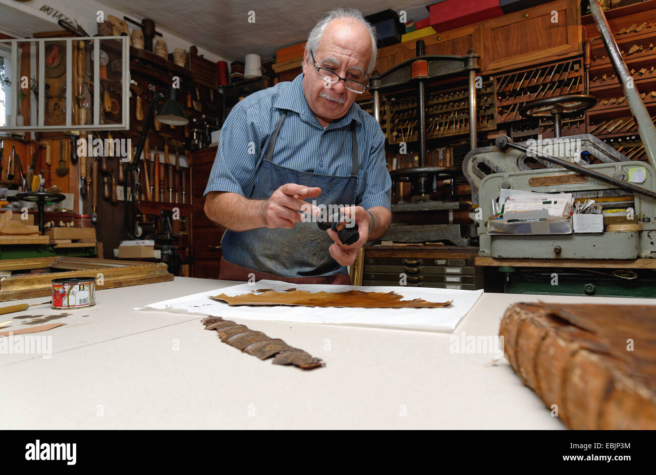 Senior man repairing fragile book spine in traditional bookbinding