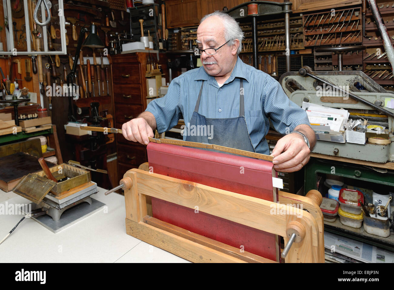 Senior man measuring book spine in traditional bookbinding workshop ...