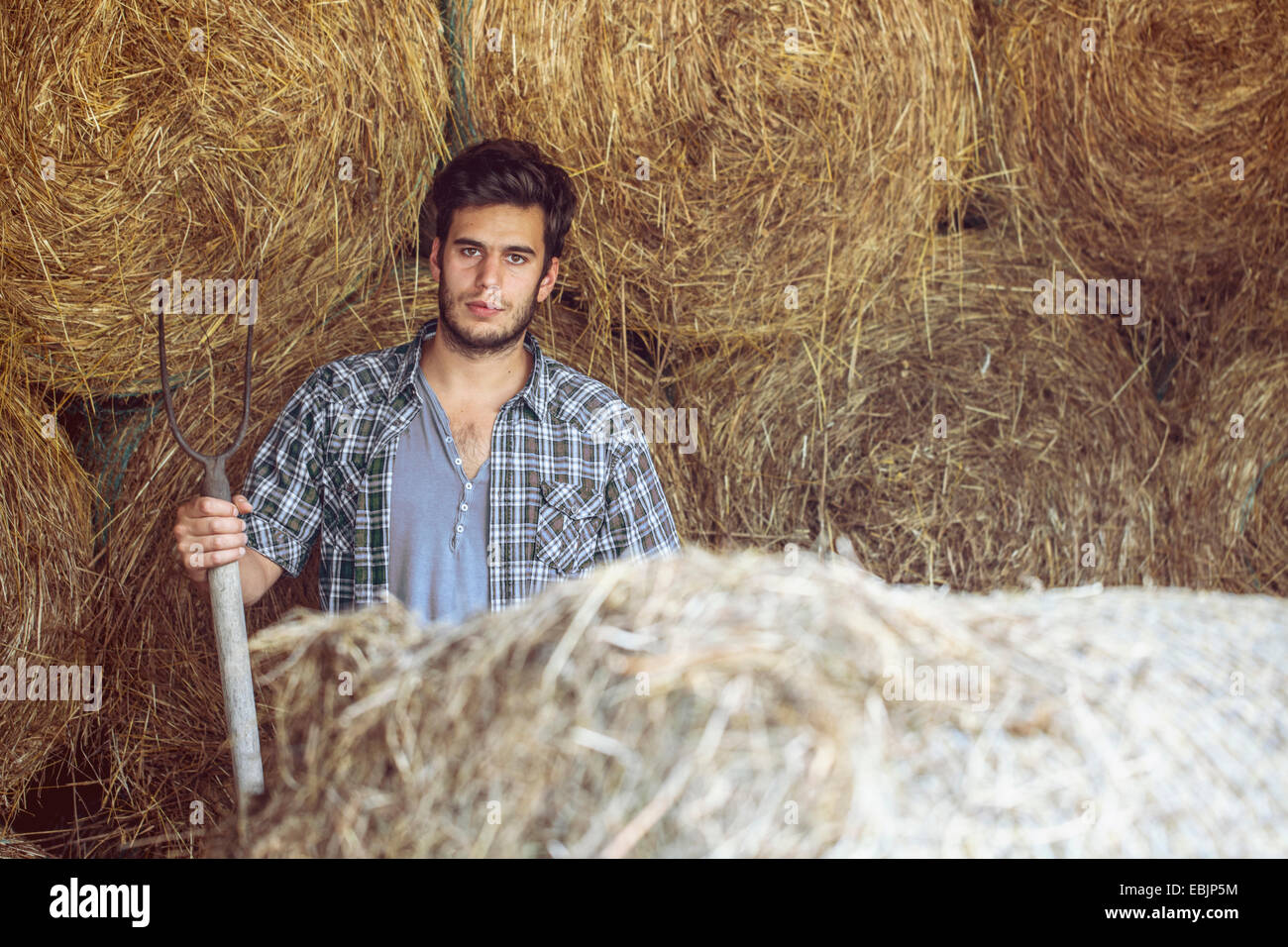 Portrait of young male farmer in straw barn with pitchfork, Premosello, Verbania, Piemonte, Italy Stock Photo