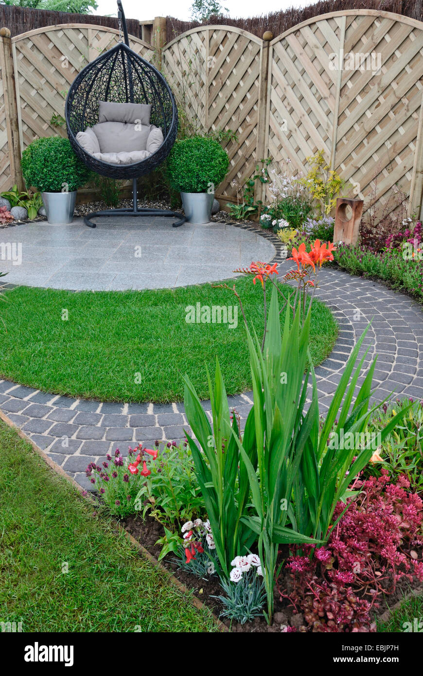 A garden design based on flowing curves around a patio area with a hanging cane chair Stock Photo