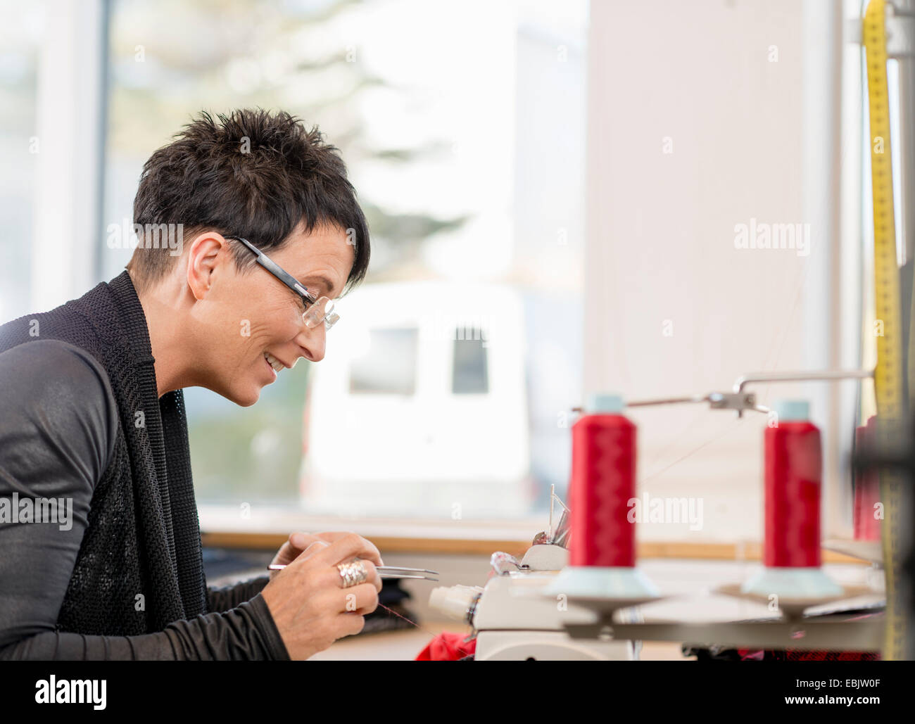 Mature seamstress picking sewing thread with tweezers in workshop Stock Photo