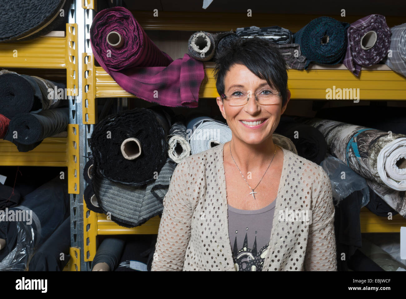 Portrait of mature seamstress in front of rolls of textile in workshop Stock Photo