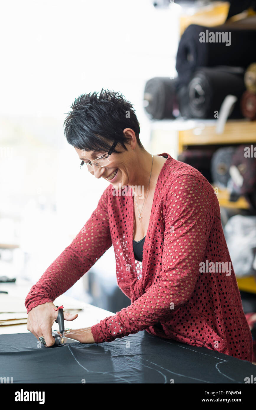 Mature seamstress using scissors to cut textile at work table Stock Photo