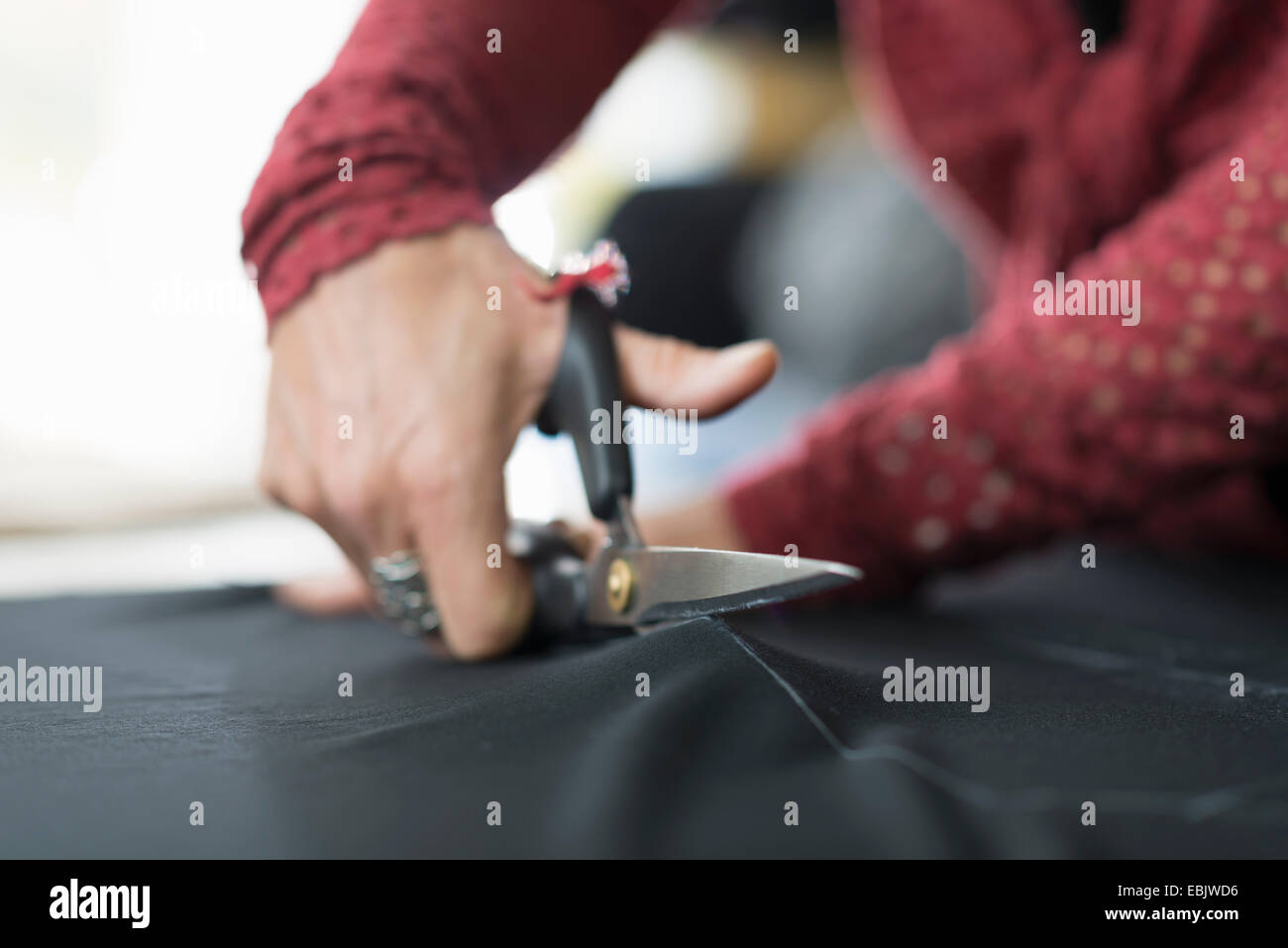 Close up of seamstress hands using scissors to cut textile at work table Stock Photo