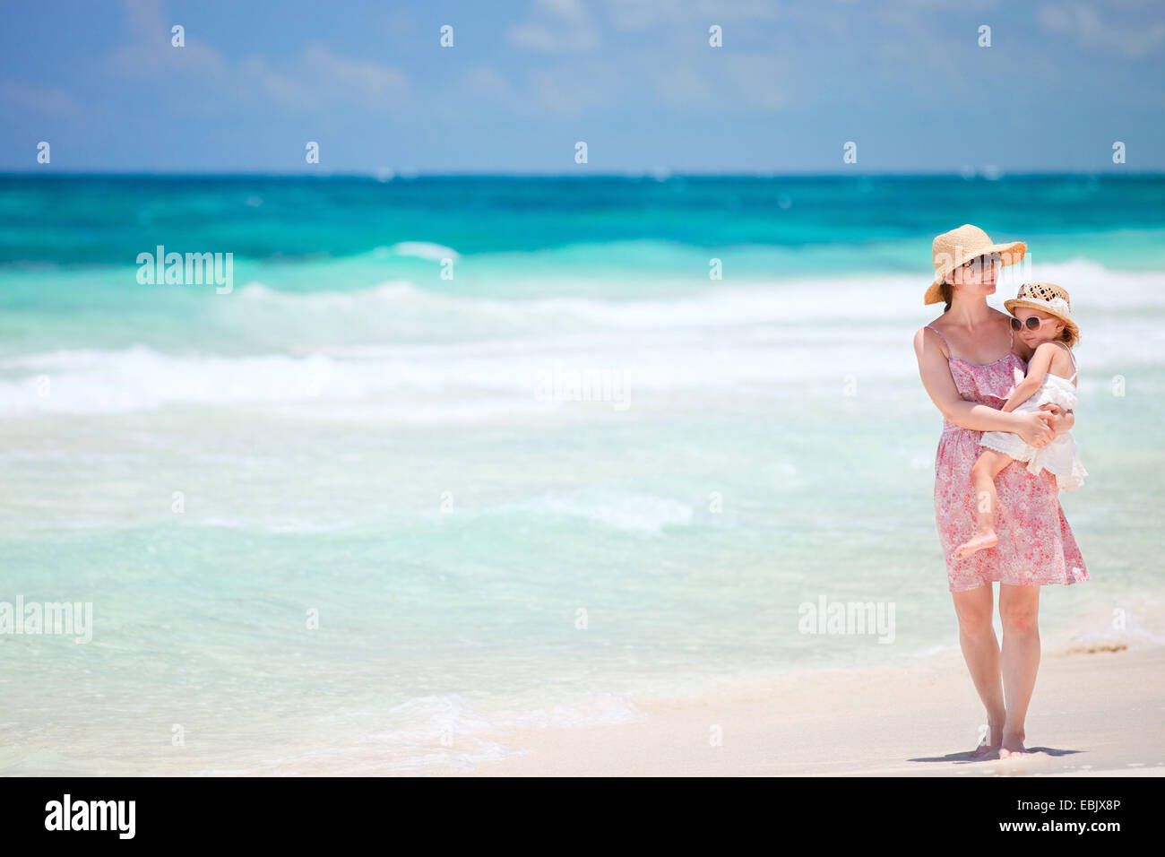 mother holding her little daughter on arm and walking on sandy beach, Mexico Stock Photo