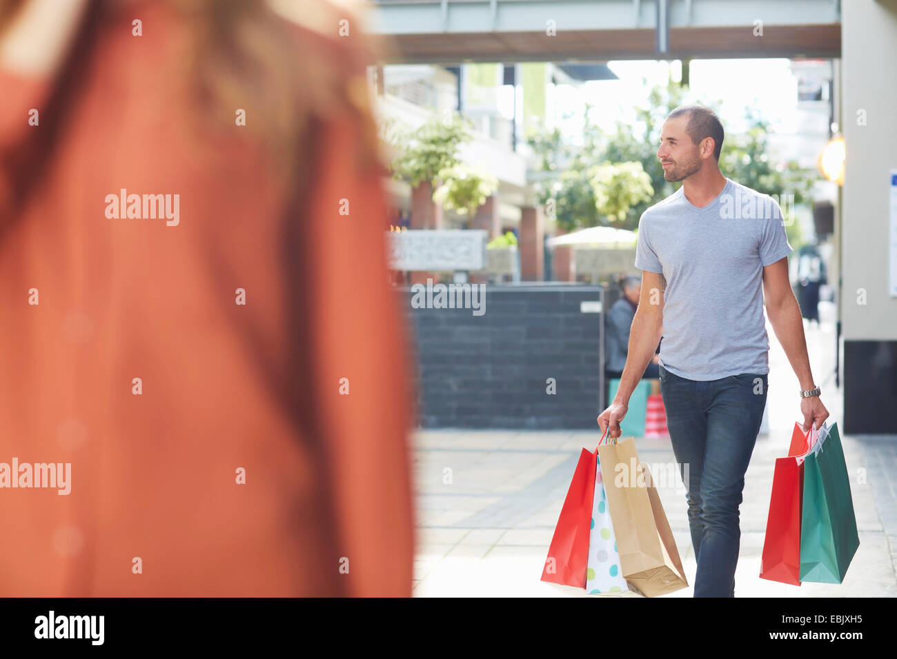 Mid adult man holding shopping bags, walking behind woman Stock Photo