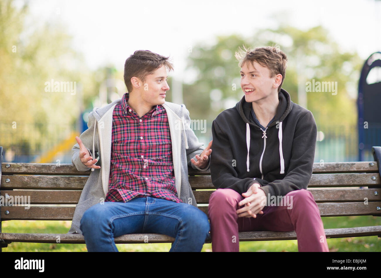 Two young male friends chatting on park bench Stock Photo
