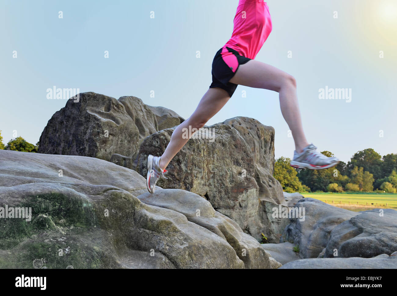 Neck down view of young female runner jumping over rock formation Stock Photo