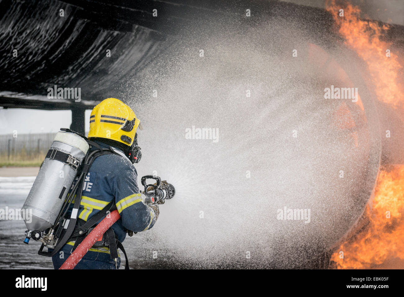 Fireman spraying water on simulated aircraft fire at training facility Stock Photo