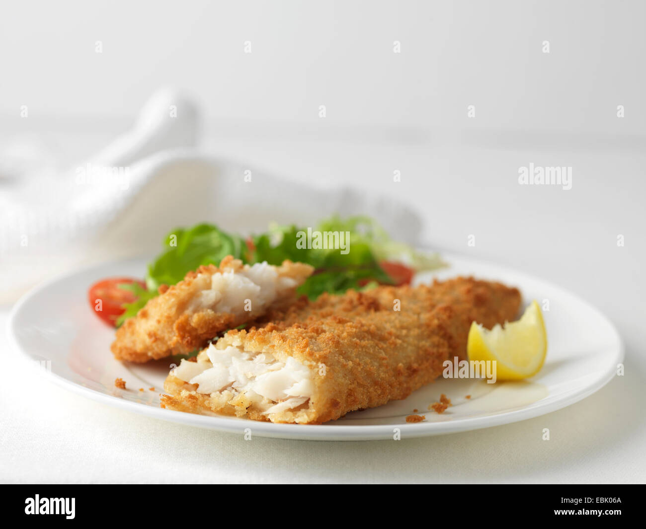 Plate of battered cod with green salad, cherry tomatoes and lemon slice Stock Photo