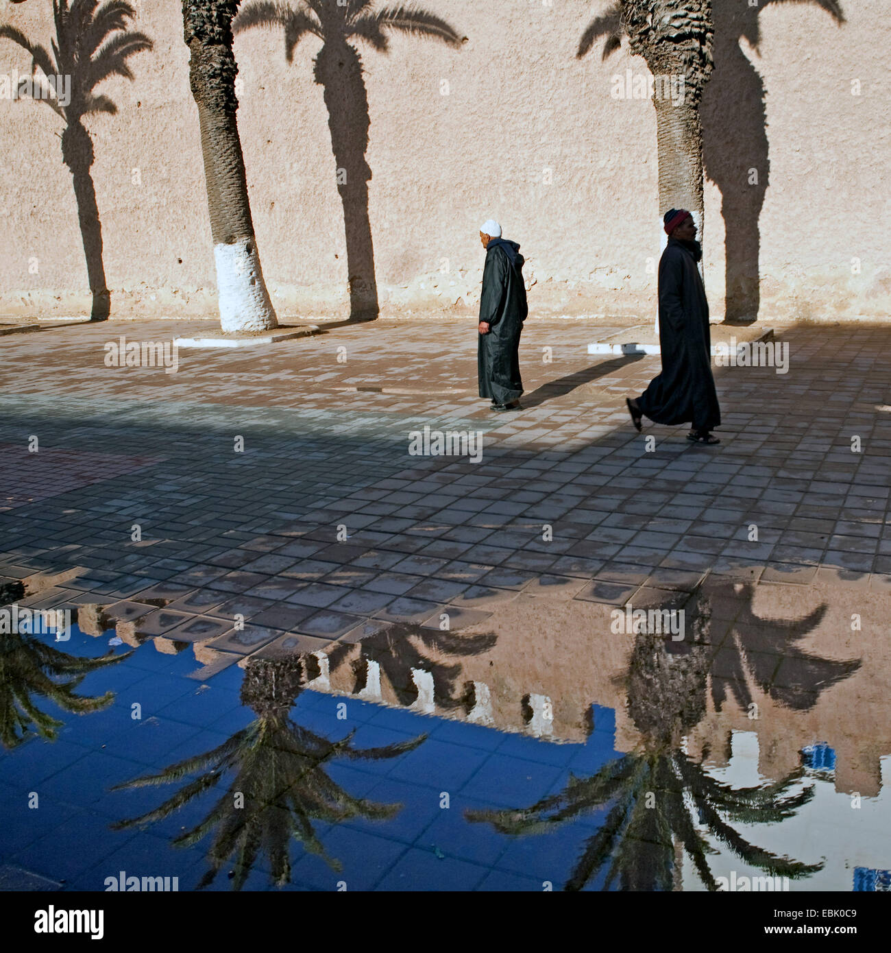 pedestrians an historical town wall reflecting in puddle of water after a ain shower, Morocco, Essaouira Stock Photo