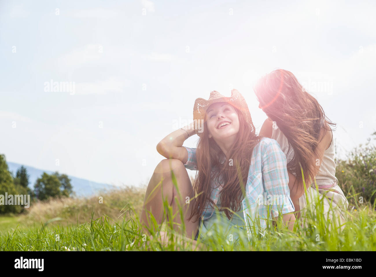 Two young women sitting chatting in grassy field Stock Photo