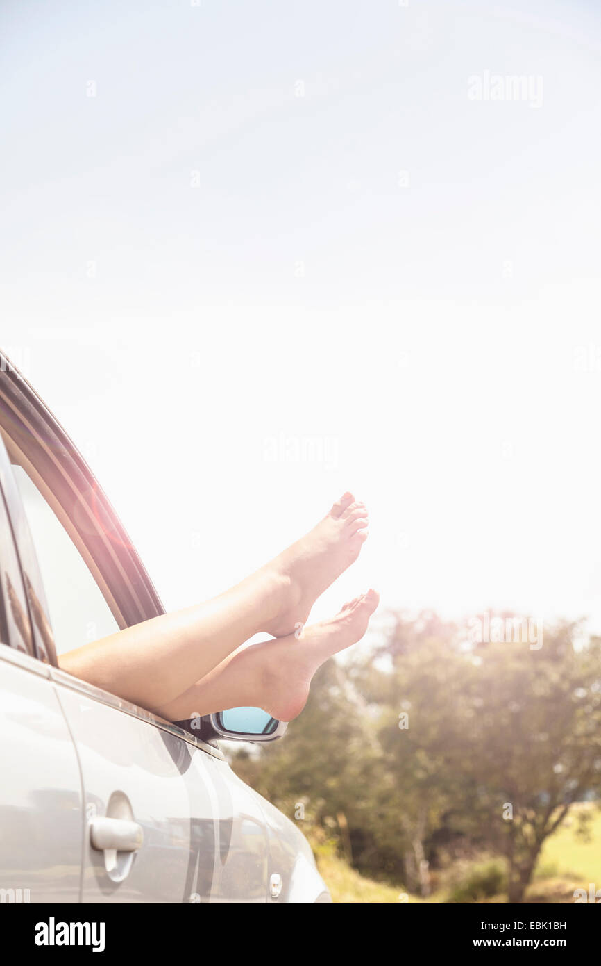Young womans bare feet resting on car window Stock Photo