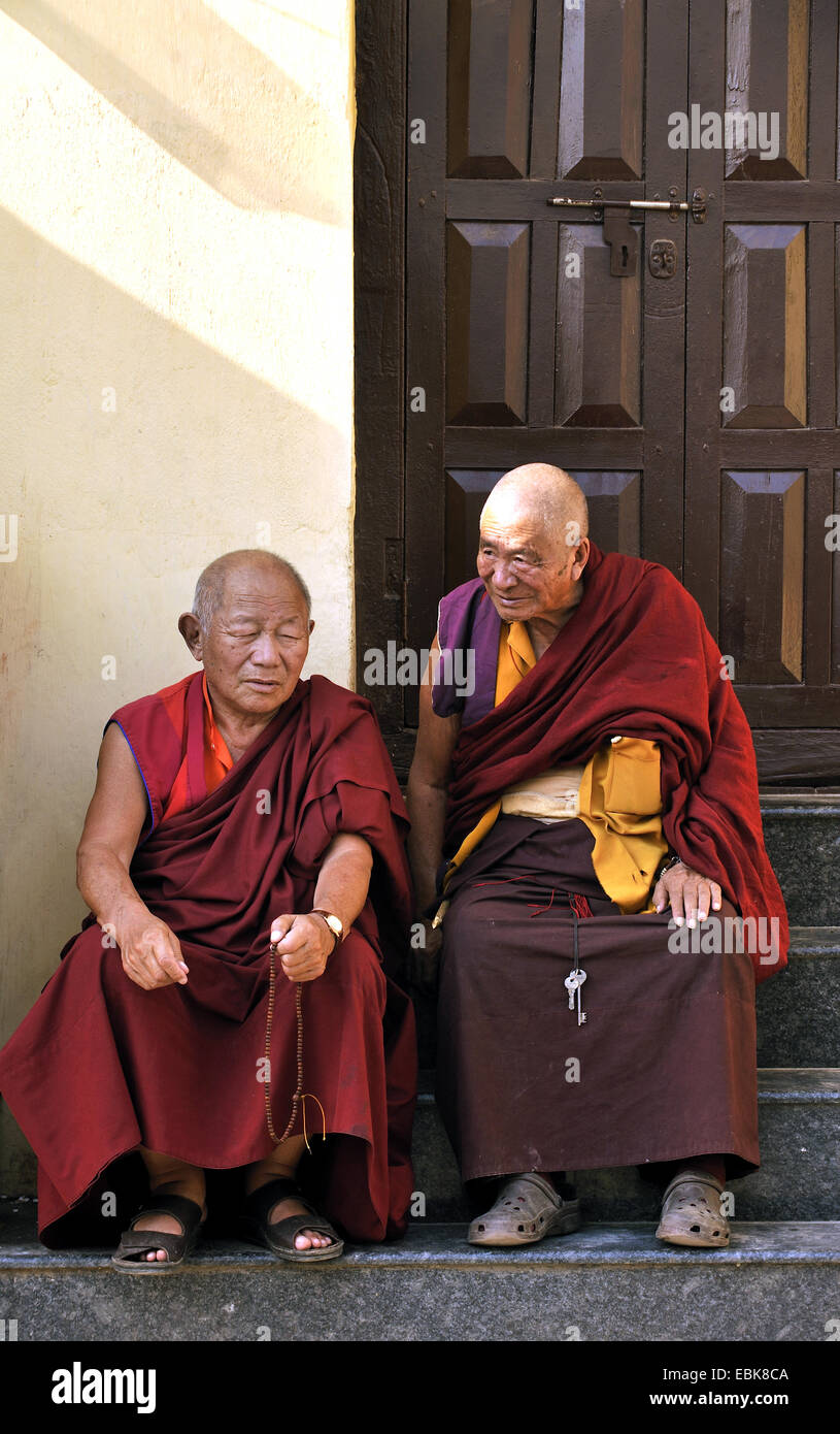 two old monks on the stairs in front of an entrance in Swayambhunath, an ancient religious complex atop a hill west of the city, Nepal, Kathmandu Stock Photo