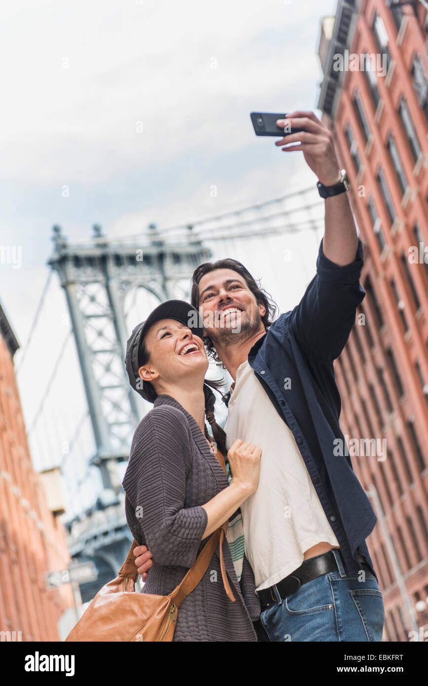 USA, New York State, New York City, Brooklyn, Couple taking selfie on street, Brooklyn Bridge in background Stock Photo