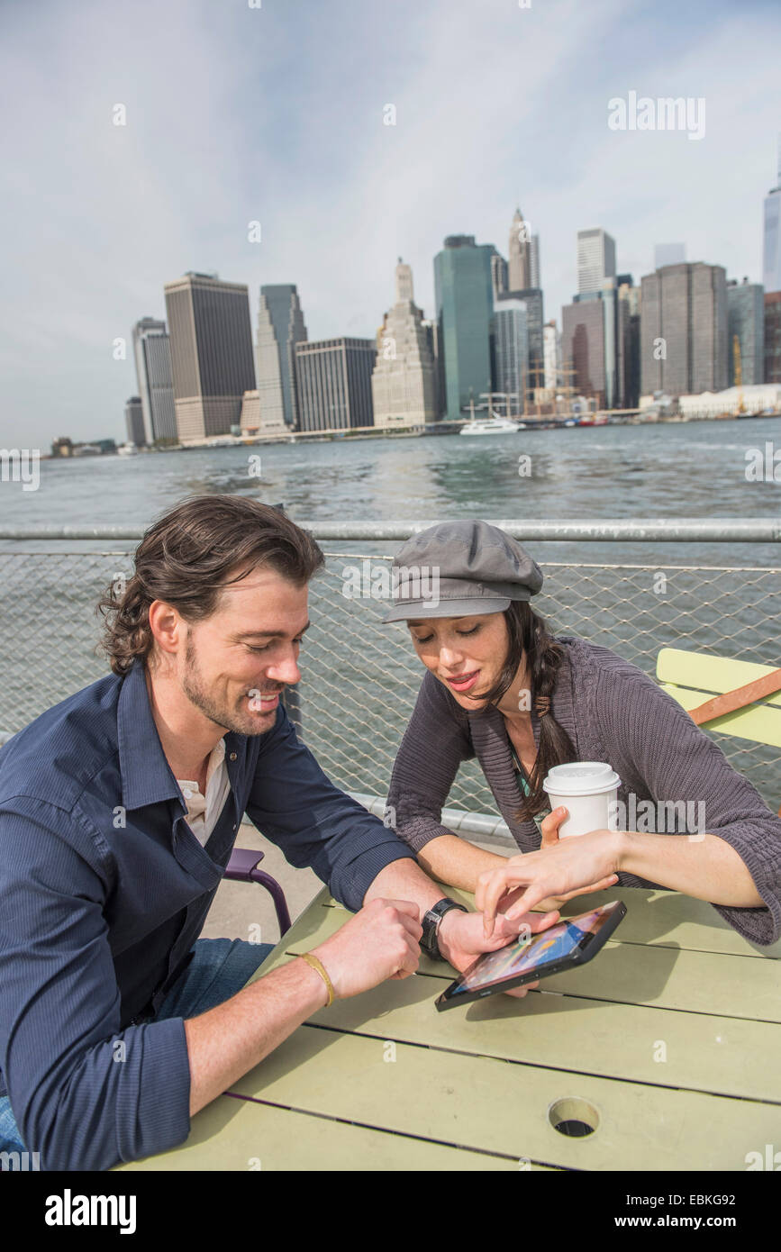 USA, New York State, New York City, Brooklyn, Happy couple sitting and using tablet pc with cityscape in background Stock Photo