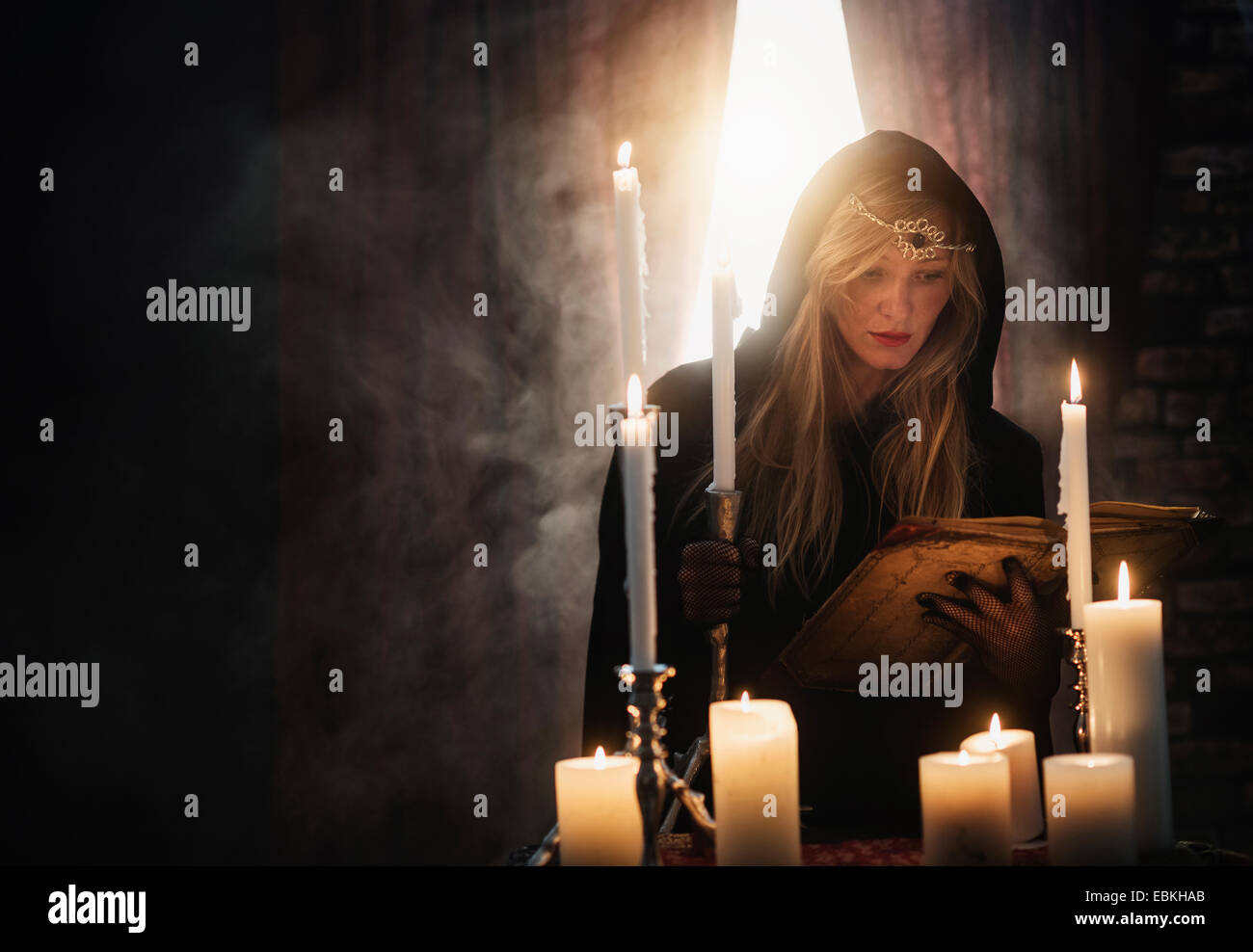 Sorceress reading book in dark room Stock Photo