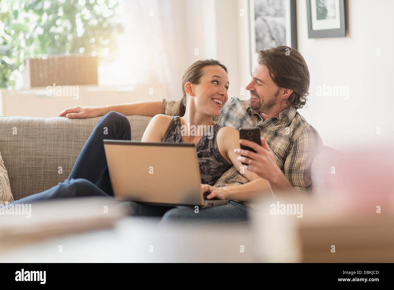 Cheerful couple on sofa with laptop and mobile phone Stock Photo