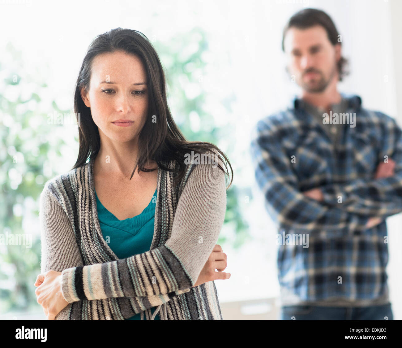 Sad woman with arms crossed, man in background Stock Photo