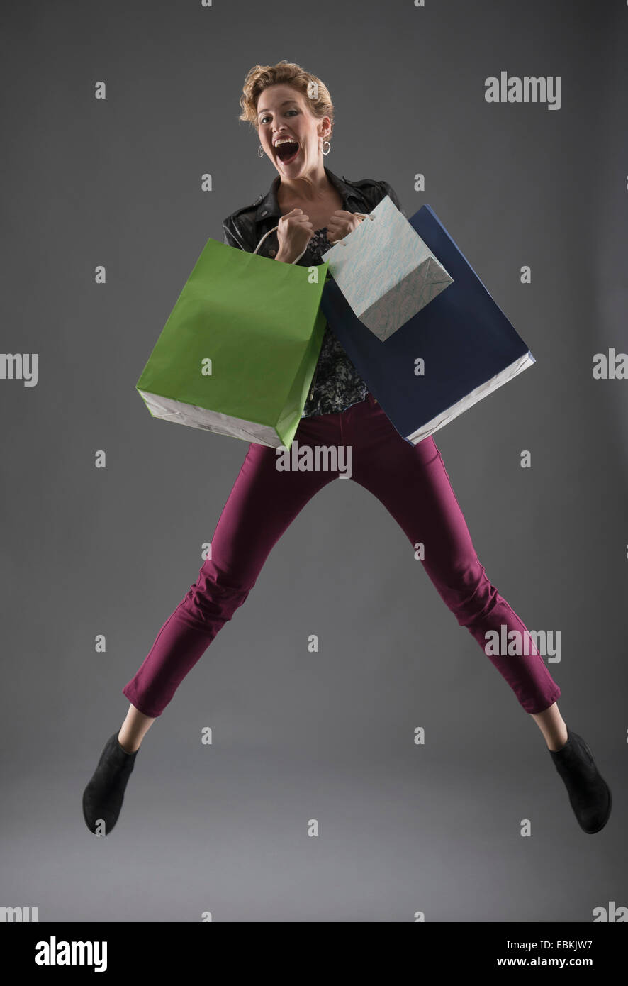 Studio shot of woman jumping with shopping bags Stock Photo