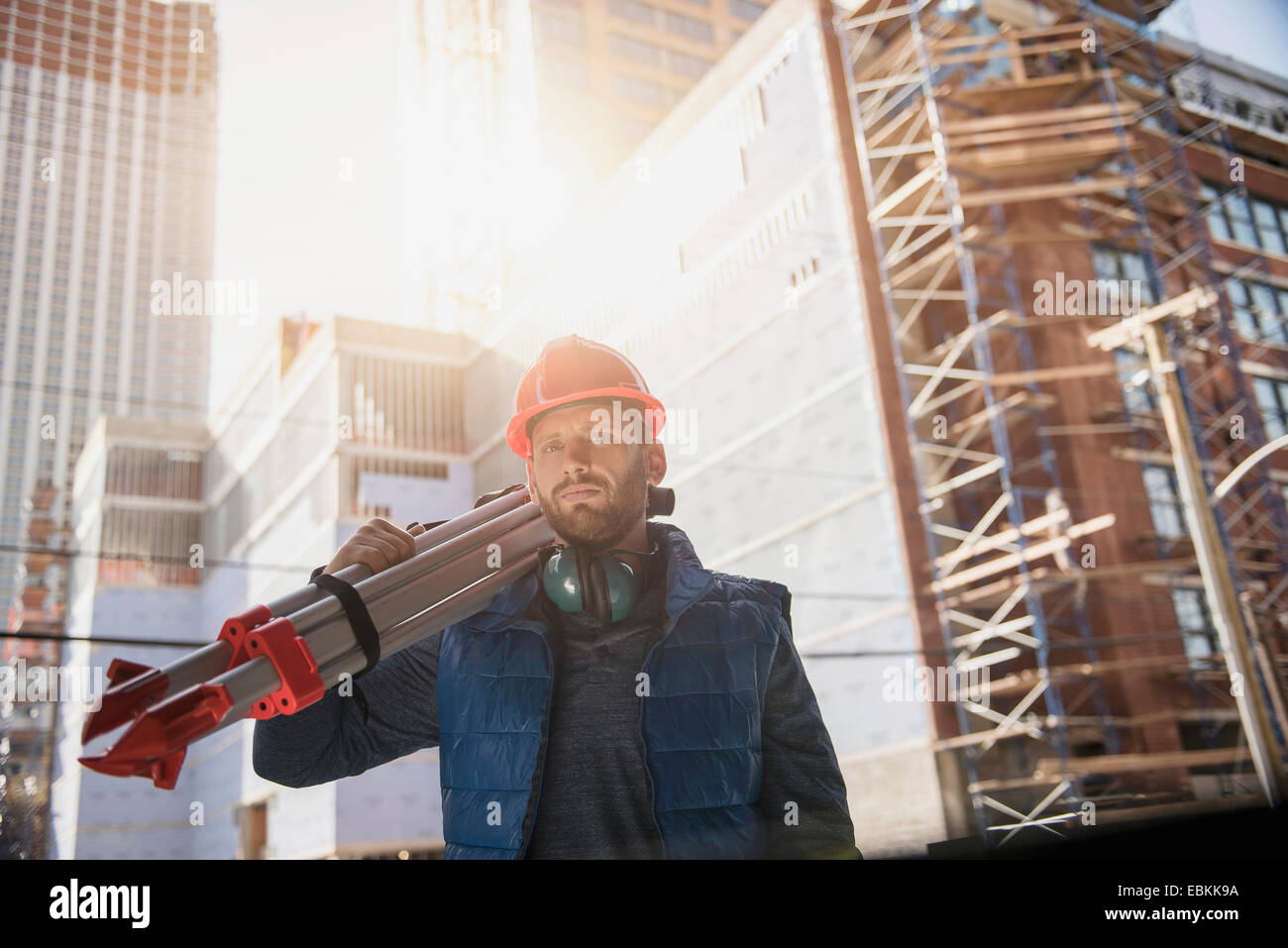 Construction worker carrying tripod on shoulder Stock Photo