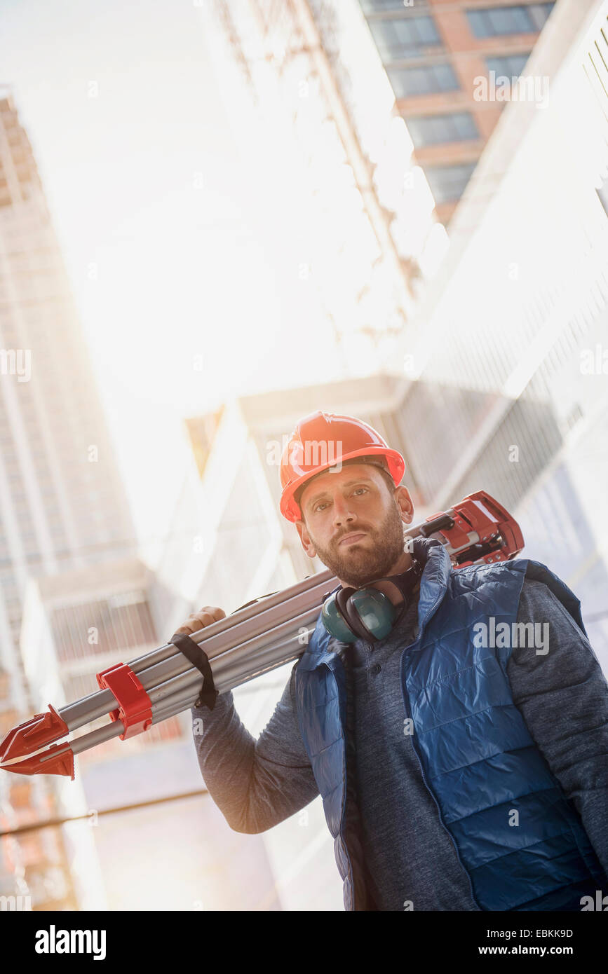 Portrait of construction worker carrying tripod on shoulder Stock Photo