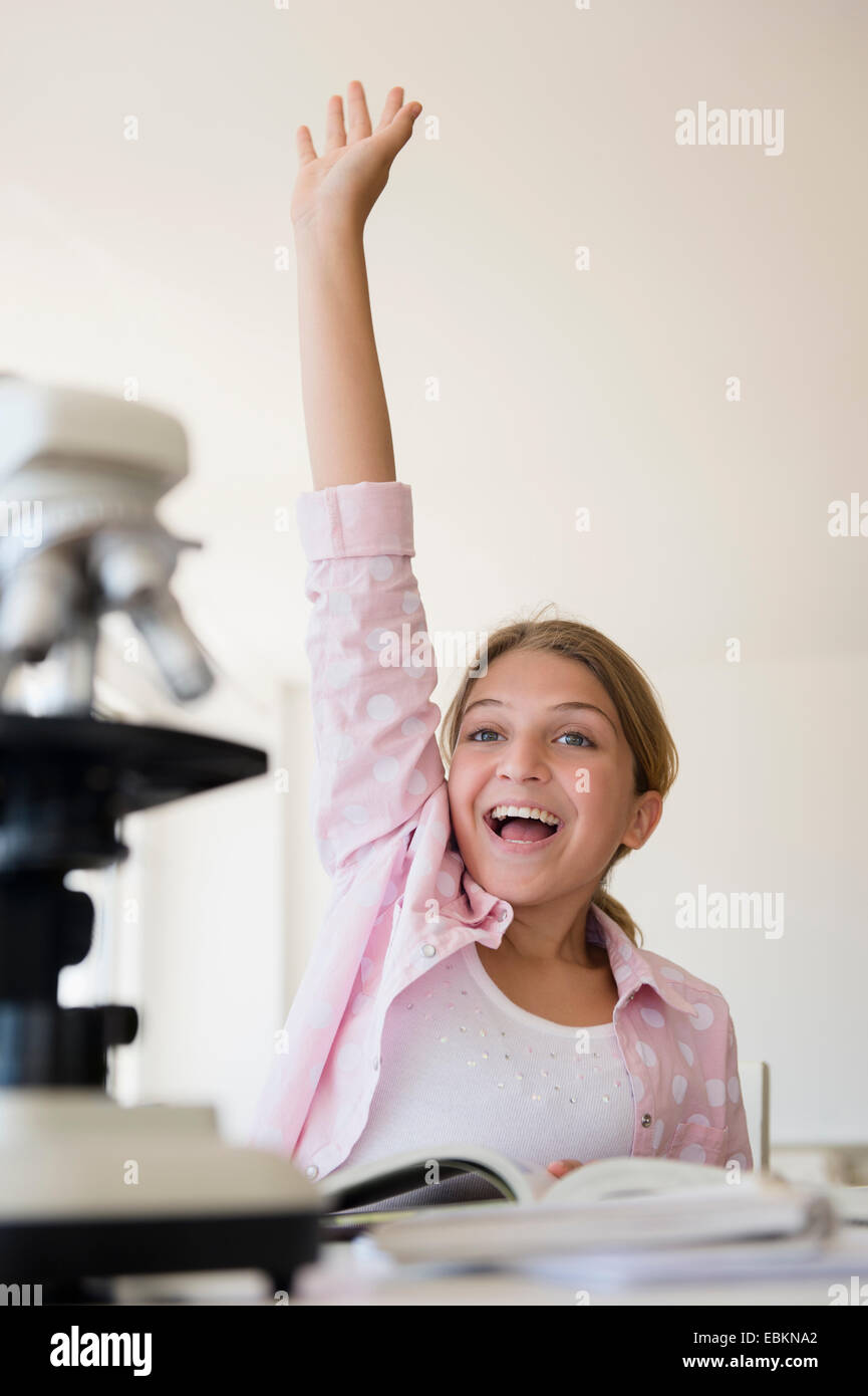 Girl (12-13) raising hand to answer question at school Stock Photo