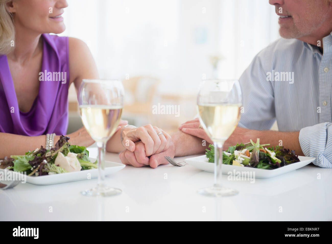 Cropped view of couple holding hands in restaurant with glasses of white wine in foreground Stock Photo