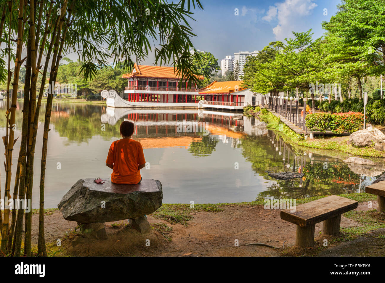 Visitor sitting on stone bench and looking out over lake to stone boat in Singapore Chinese Garden Stock Photo