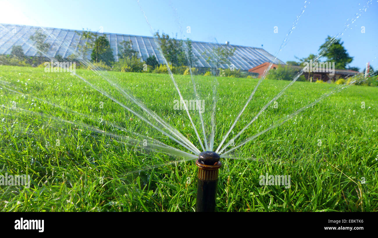 spray irrigation on a lawn, house with solar collectors on the roof