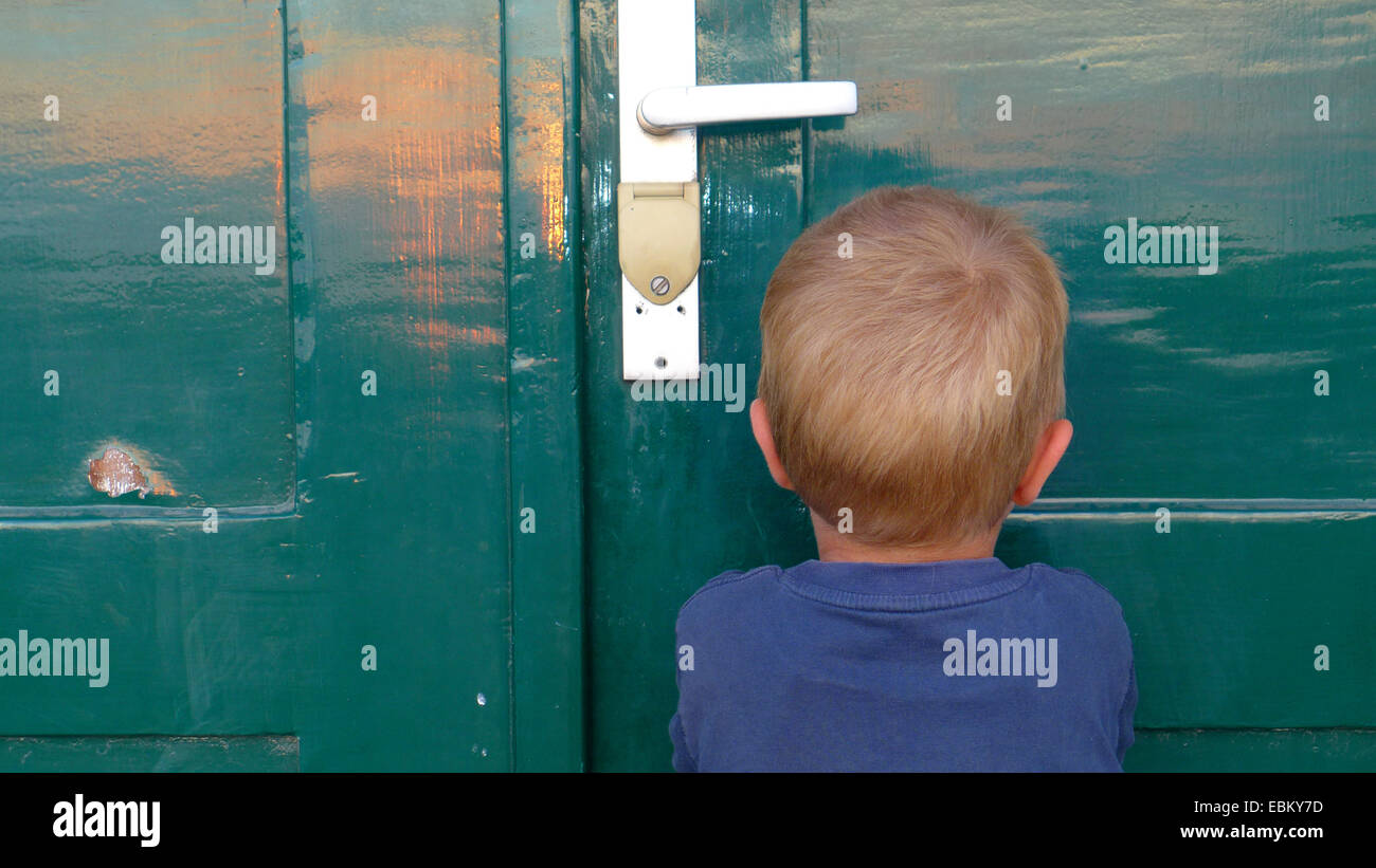 young boy standing in front of closed door sulking, Germany Stock Photo