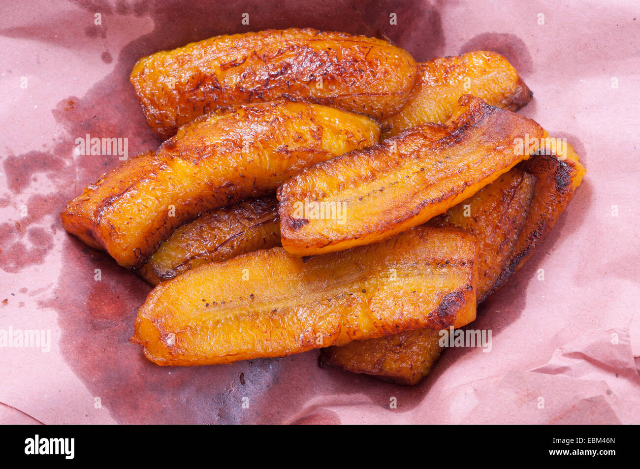 Sliced greasy fried plantain bananas on pink paper to soak up excess