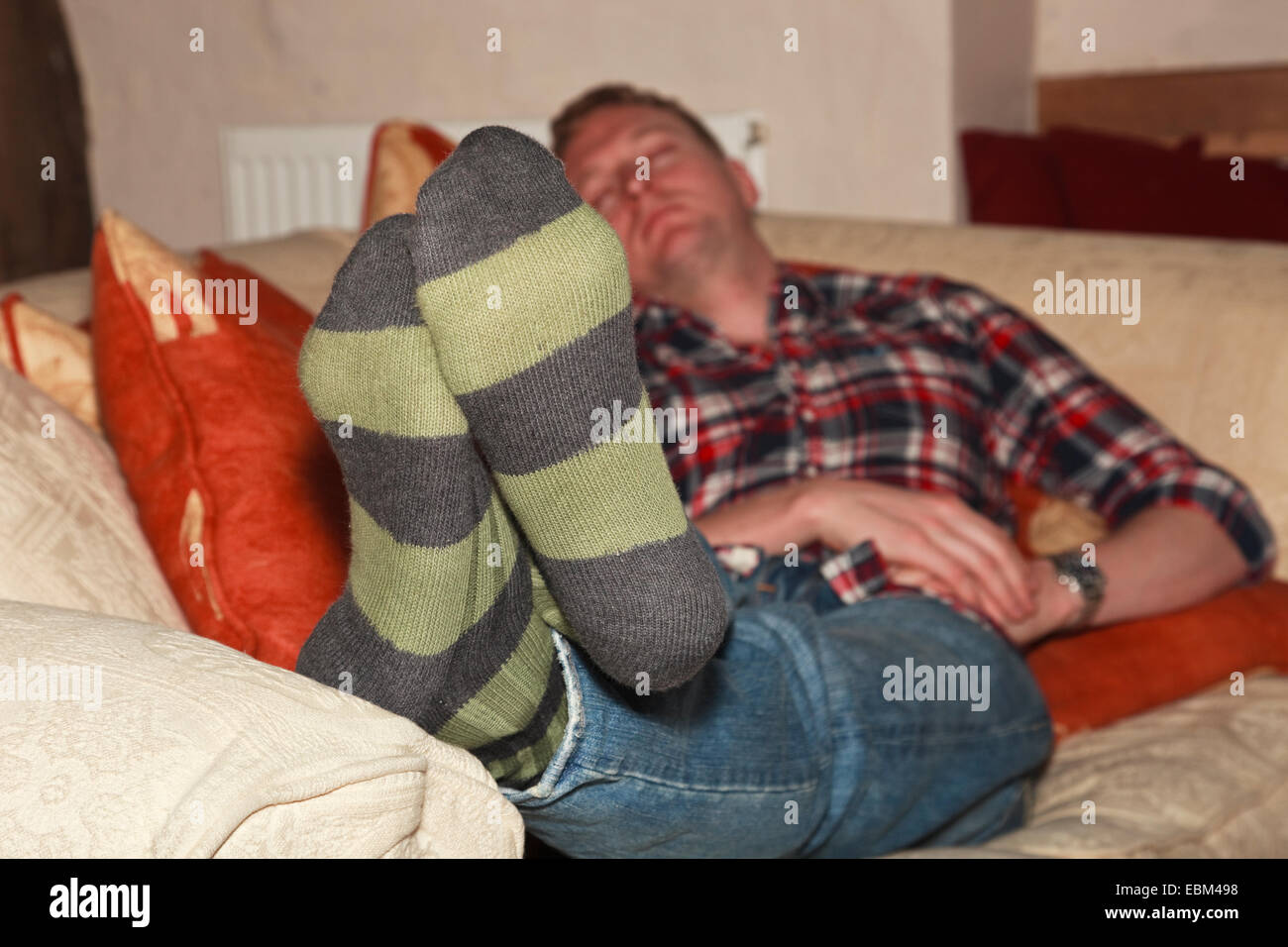 A tired young man needing more sleep sleeping on a living room sofa at home. England UK Britain. Stock Photo