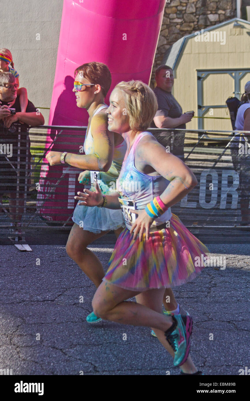 Man and woman runners splattered with colorful dye race together in the