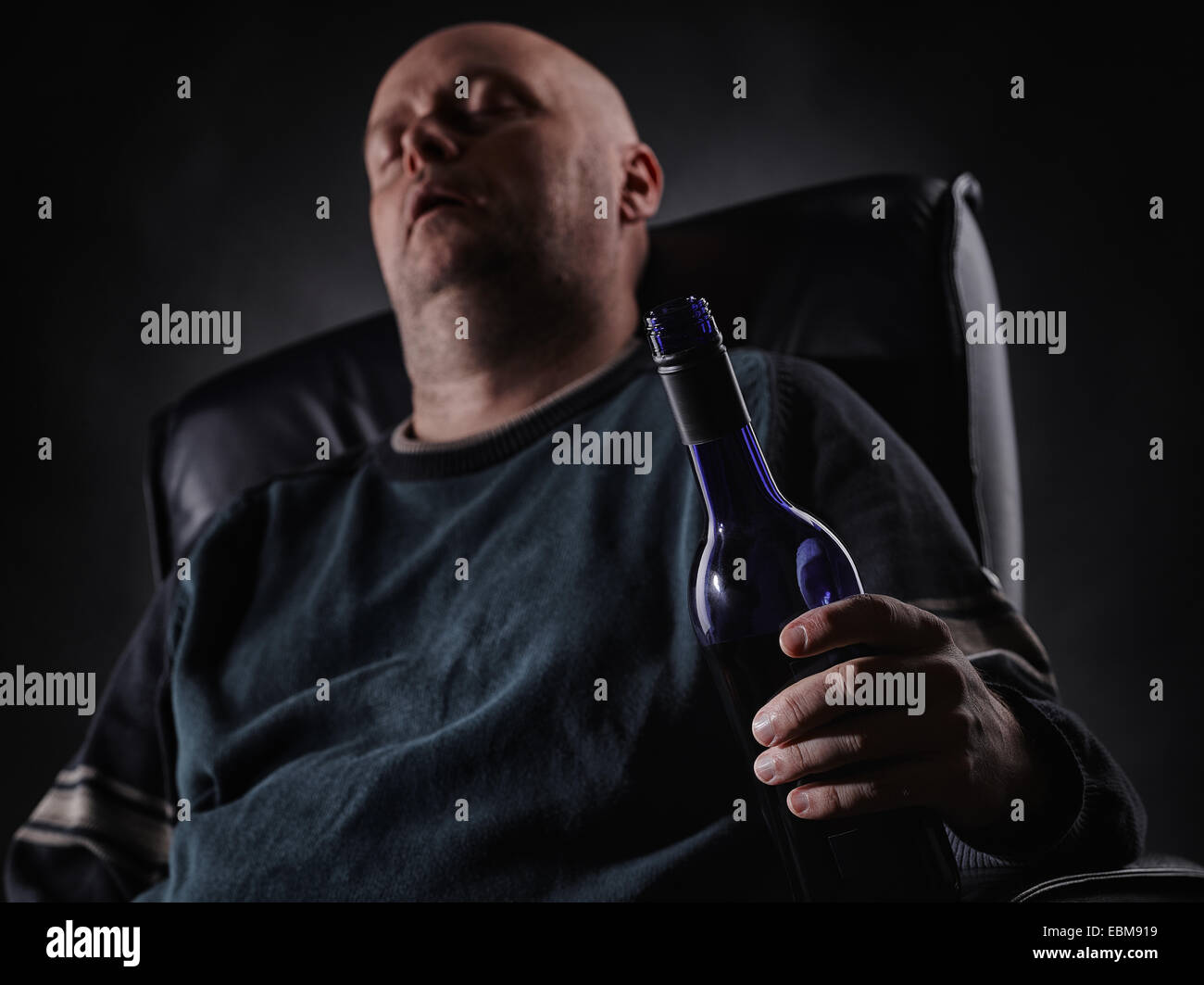 Middle aged man sleeps on an armchair and he holding a wine bottle, horizon format Stock Photo